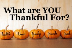 Five thankful oange pumpkins sit in a row in front of a distressed, wooden background.