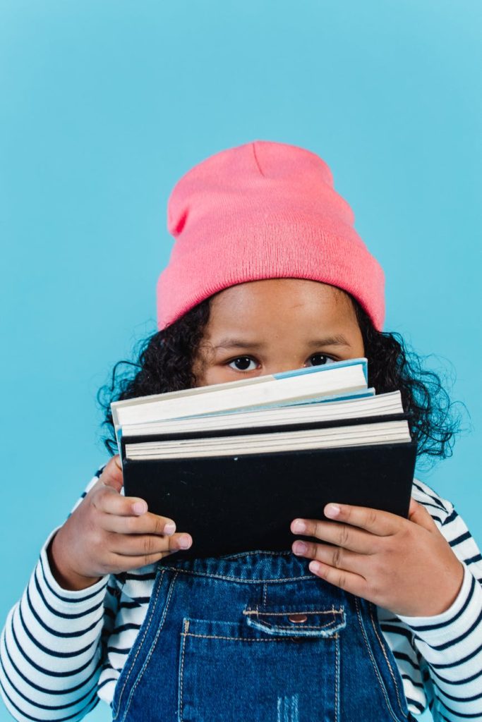 focused black girl holding book near face in studio